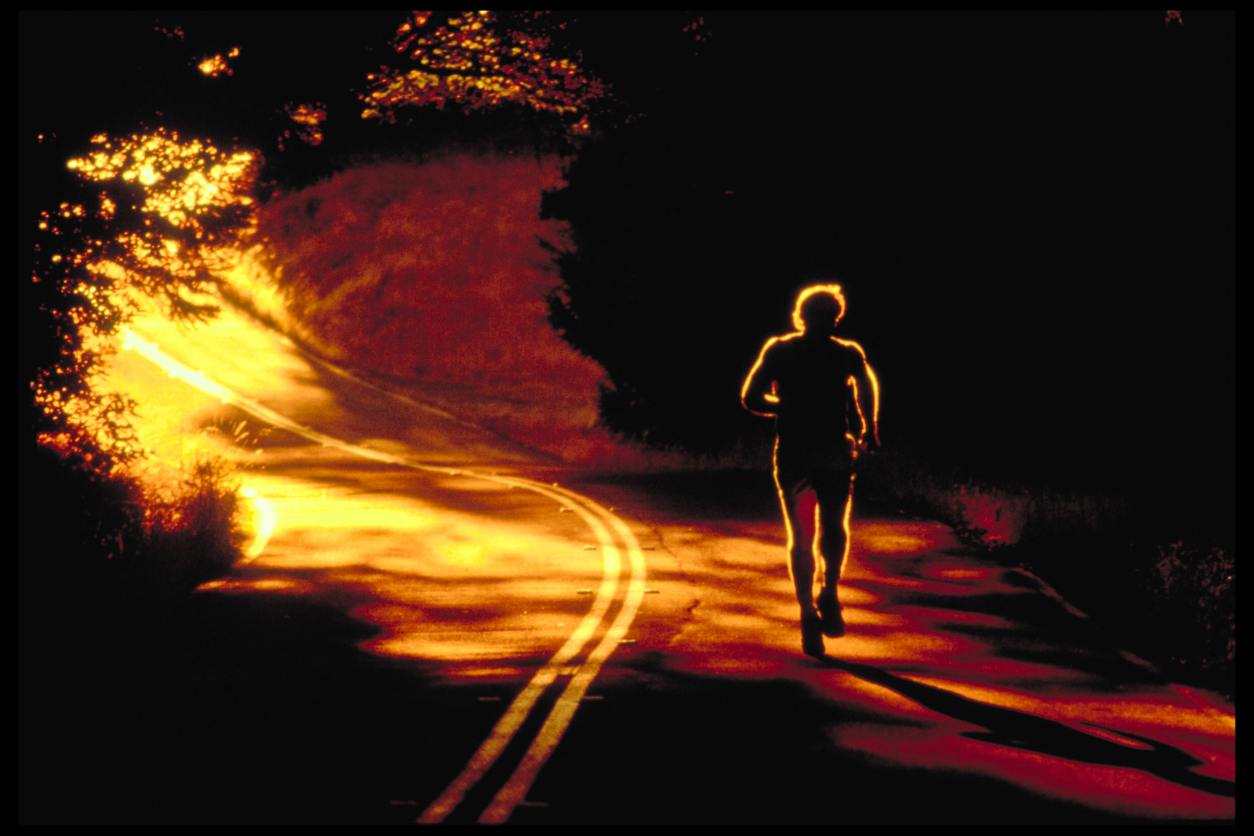 Silhouette of a man running down a road at night illuminated by streaks of golden light
